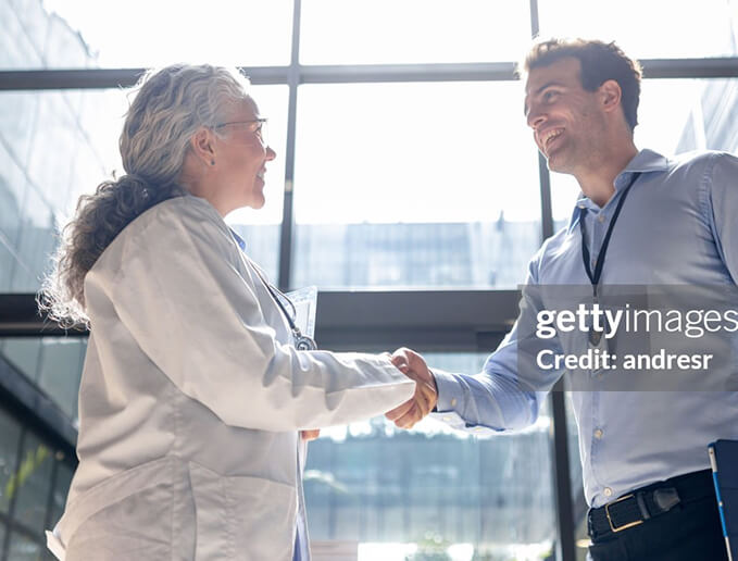 Scientist in a lab coat shaking hands with a professional in a bright, modern building